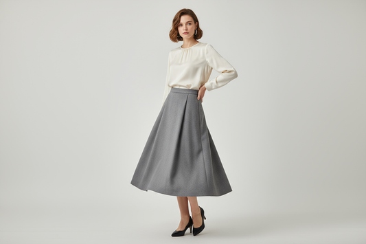 A woman in her twenties Cut from fine grey suiting wool, The Vale Skirt mirrors the blazer’s quiet structure and fluid movement. Its tailored shape falls with ease, creating a silhouette that feels refined yet effortless. Designed to pair seamlessly with The Vale Blazer, reflecting Azaleia’s vision of understated elegance and timeless form.